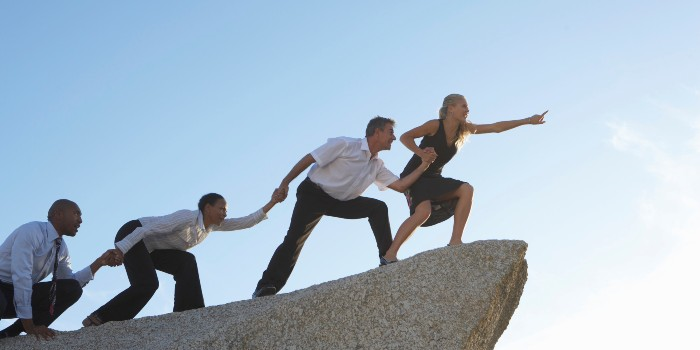 Woman leading three colleagues on rock, pointing