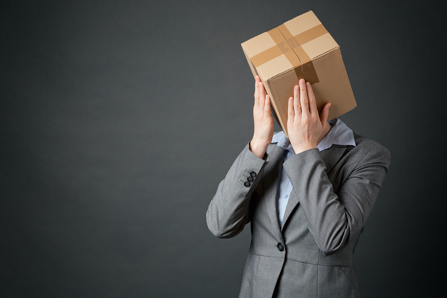 A failing businesswoman wearing a box over her head holds her hands before her face.